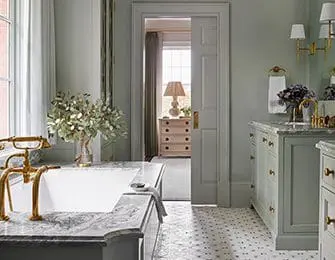 Light green bathroom with marble tub, brass fixtures, and tiled floor.