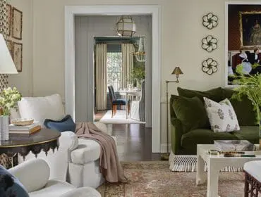 Living room with green velvet sofa, white slipcovered chairs, and view into dining room.