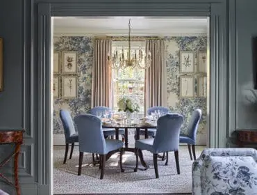 Dining room with blue floral wallpaper, light blue chairs around a round table, and a chandelier.