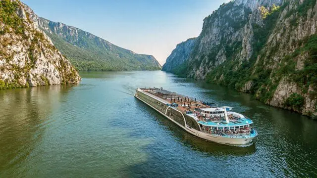 AmaMagna cruise ship on the Danube River between steep, green, rocky cliffs.