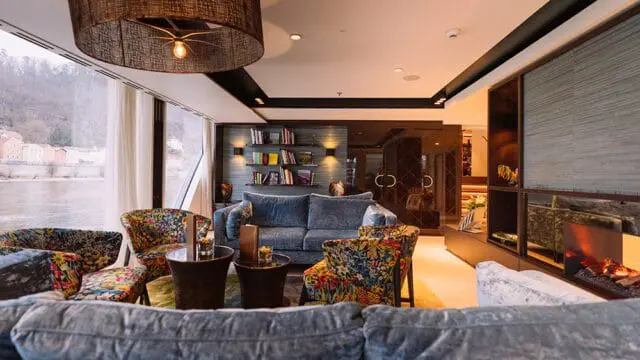 Blue sofa and floral chairs in a library with a fireplace and view of a river