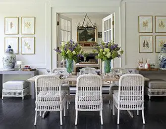 Dining room with wicker chairs, light wood table, and botanical prints on walls.