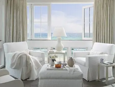 White living room with slipcovered chairs and ottoman overlooking the ocean