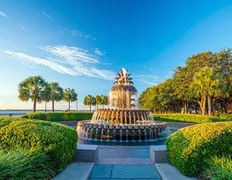 Pineapple fountain surrounded by manicured bushes and palm trees under a bright blue sky