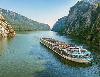 River cruise ship sailing through a gorge with steep, tree-covered cliffs on either side.