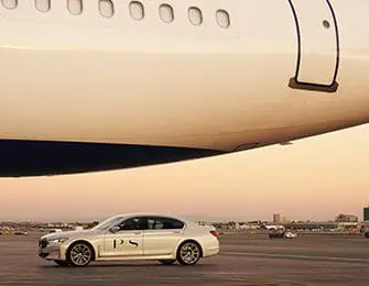 White sedan with PS logo parked on tarmac under airplane wing