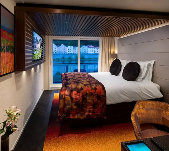 Bedroom with a bed, orange and red patterned blanket, and a view of a town across water.