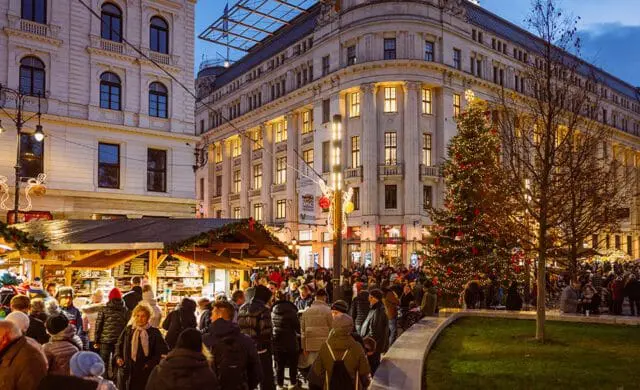 Christmas market with stalls and a large decorated tree in front of ornate buildings at dusk