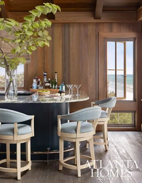 Bar with light blue upholstered stools, granite countertop, and wood paneled walls overlooking the