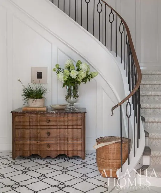 Foyer with antique wooden chest, floral arrangement, curved staircase with black railing, and