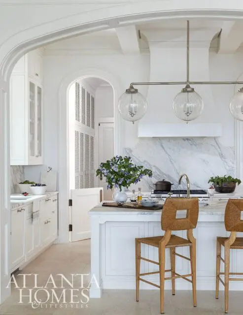White kitchen with marble backsplash, island, and woven bar stools.