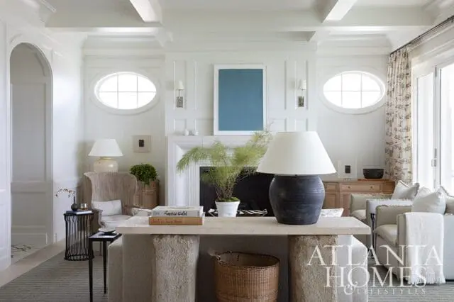 Living room with white paneled walls, oval windows, fireplace, and light neutral furniture.