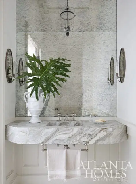 Powder room with marble vanity, white urn with plant, and mirrored wall