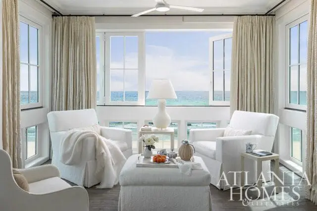 Seaside primary bedroom seating area with white slipcovered chairs and ottoman overlooking the