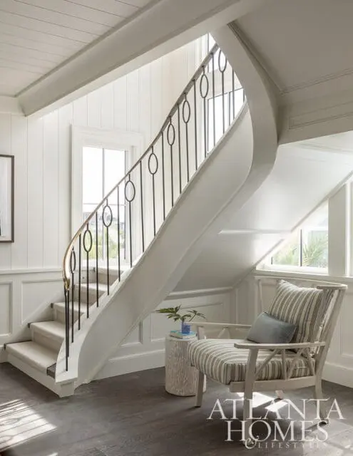 Curved staircase with black railing, carpeted stairs, and striped armchair.
