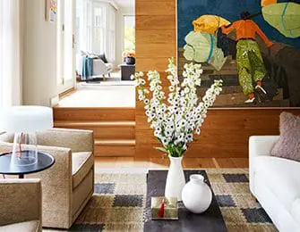 Living room with tan chairs, white sofa, colorful art, and wood paneling.