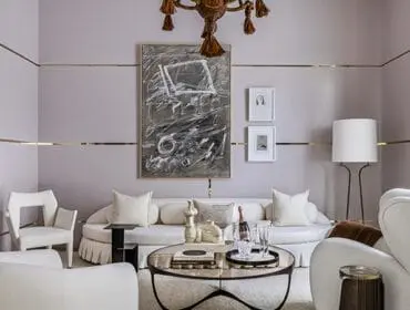 Living room with lavender walls, gold trim, white curved sofa, abstract art, and modern chairs
