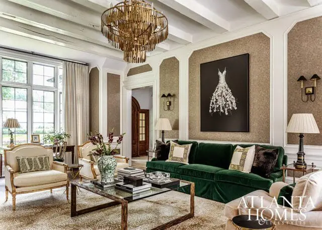 Living room with green velvet sofa, ornate chandelier, and artwork of a dress.