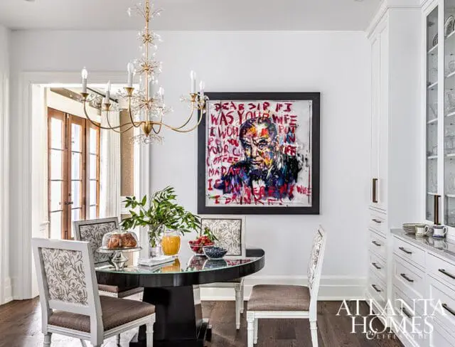 Dining area with abstract portrait, round table, and white cabinetry.