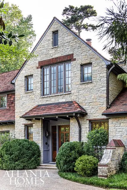 Stone house with arched entryway, multi-paned windows, and red tile roof.