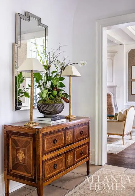 Inlaid wood dresser with two gold lamps and floral arrangement. Atlanta Homes logo.
