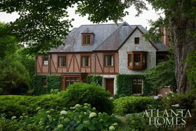 Tudor-style home with stone and brick facade, bay windows, and lush landscaping.
