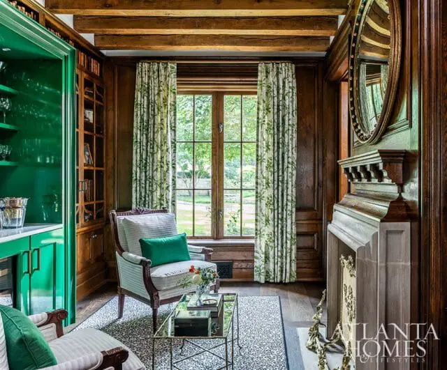 Library with green built-in cabinets, wood paneling, fireplace, and floral curtains.