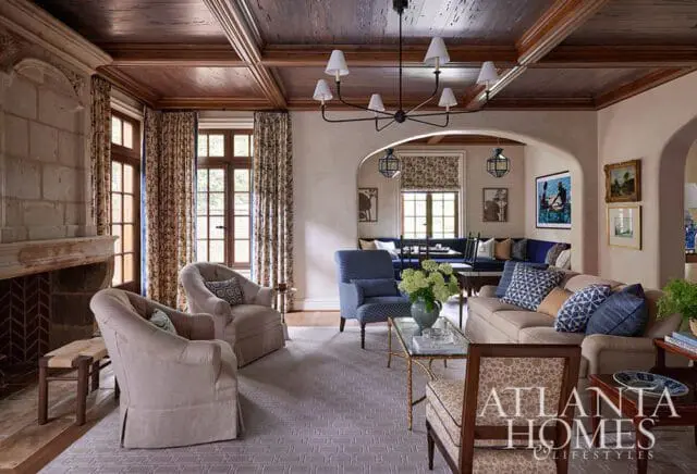 Living room with coffered wood ceiling, stone fireplace, upholstered chairs, and sofa with blue