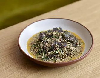 Bowl of grain salad with dark leafy greens and a creamy sauce on a wooden table.