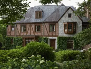 Tudor-style house with stone and brick facade, dormer windows, and lush landscaping.