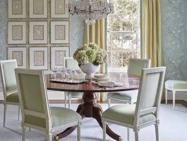 Dining room with floral wallpaper, a round wooden table, and light green upholstered chairs.
