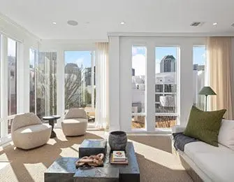 Living room with large windows, white sofa, textured chairs, and dark metal coffee table.