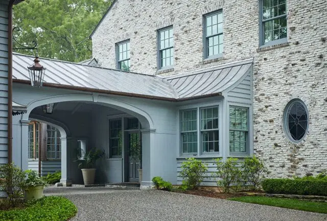 Light brick house with gray trim, metal roof, and covered entryway with arched opening.