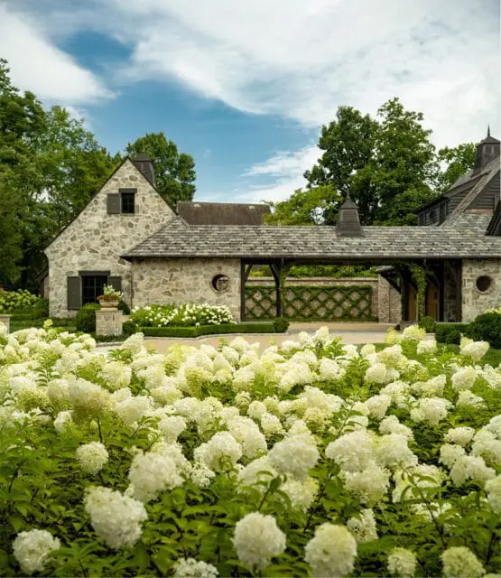 Stone estate with white hydrangeas in the foreground under a blue sky with clouds