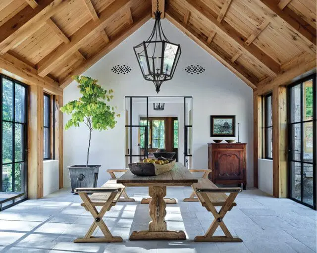 Dining room with vaulted wood ceiling, stone floor, and large windows. Rustic wood table and
