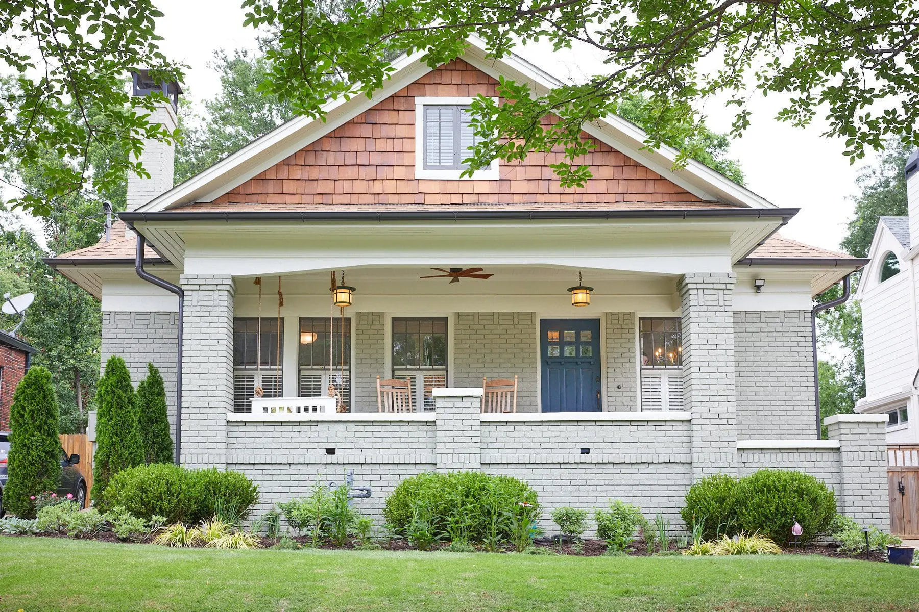 Gray brick house with a covered porch, blue front door, and cedar shake roof.