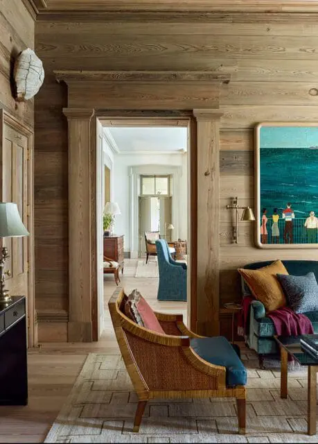 Living room with wood paneled walls, rattan chair, teal sofa, and abstract art