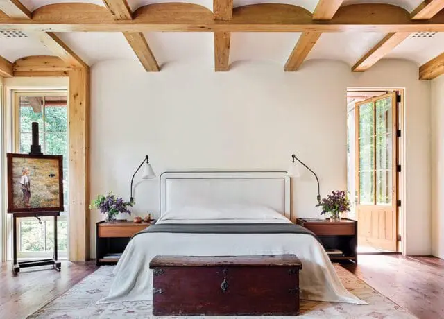 Bedroom with white upholstered headboard, wooden beams, and antique chest.