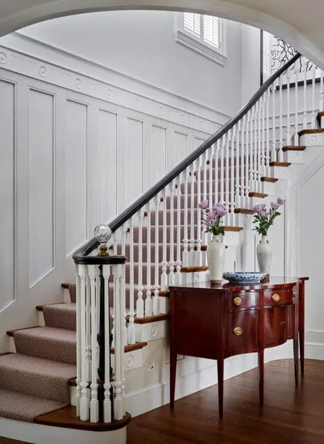 White paneled walls, carpeted stairs, dark wood console table with vases of flowers