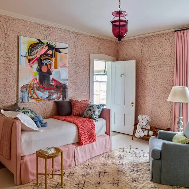 Girls bedroom with pink floral wallpaper, pink daybed, abstract art, and blue armchair.