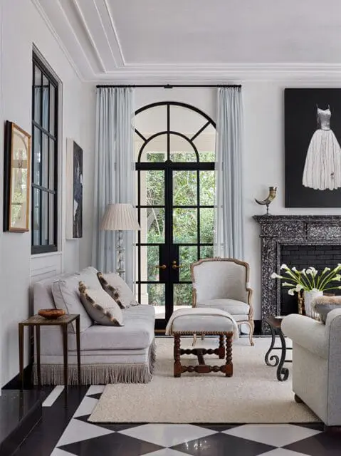Living room with light gray sofa, ornate fireplace, and arched French doors overlooking greenery.