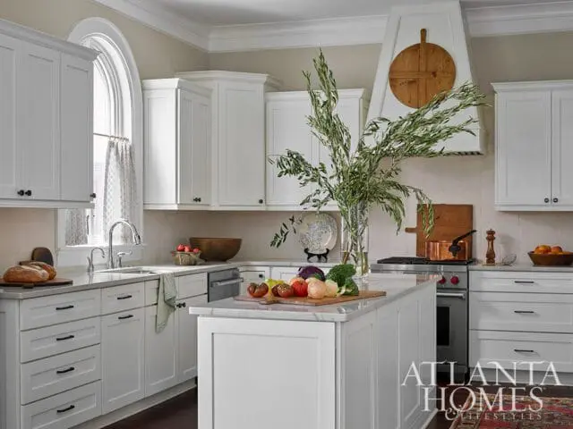 White kitchen with marble island, stainless steel appliances, and arched window.