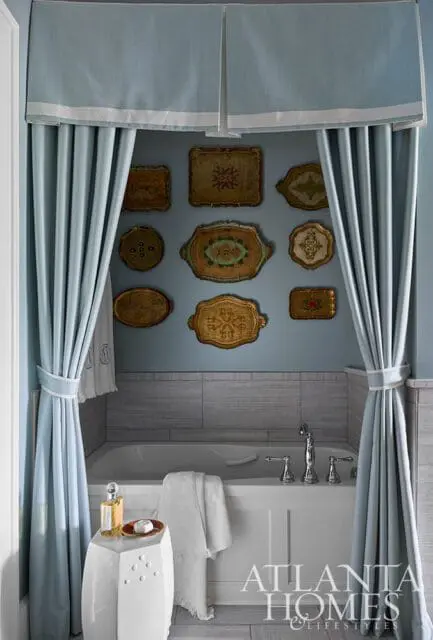 Blue bathroom with a bathtub, decorative trays on the wall, and light blue curtains.