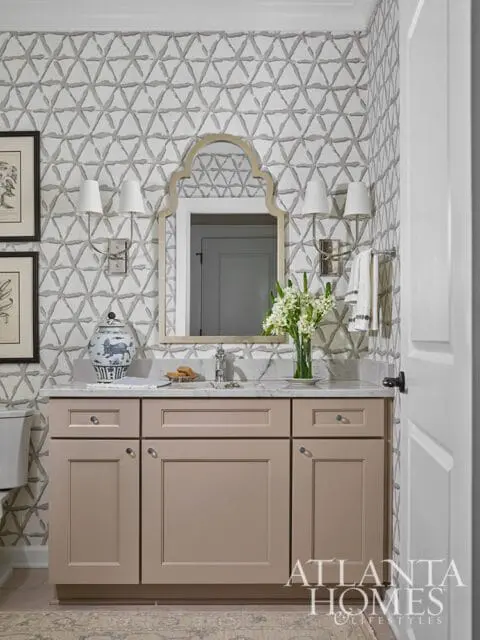 Bathroom vanity with taupe cabinets, marble countertop, and geometric wallpaper.