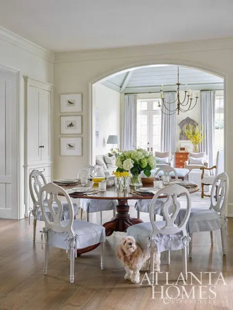 Dining room with round wooden table, upholstered chairs, and dog.