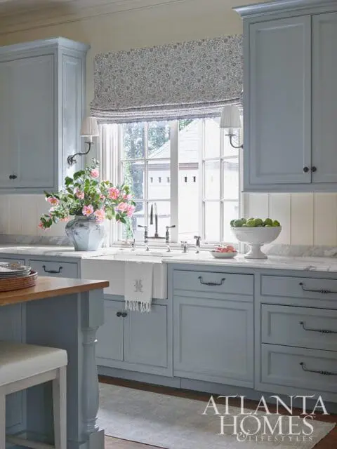 Light blue kitchen cabinets with marble countertops and a farmhouse sink.