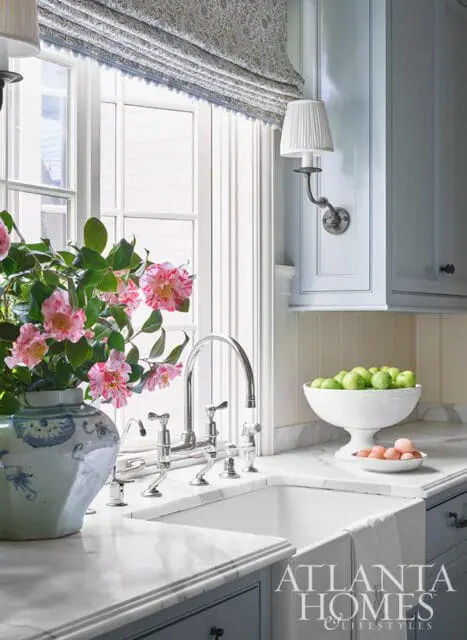Farmhouse sink with chrome faucet, marble counters, and floral arrangement.