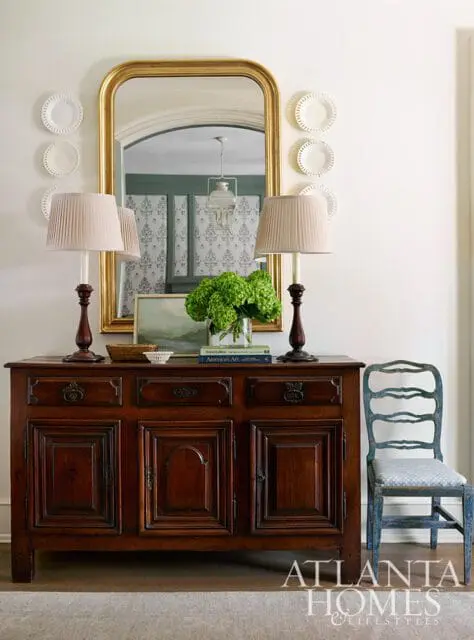 Dark wood buffet with gold mirror, two lamps, and green hydrangeas.