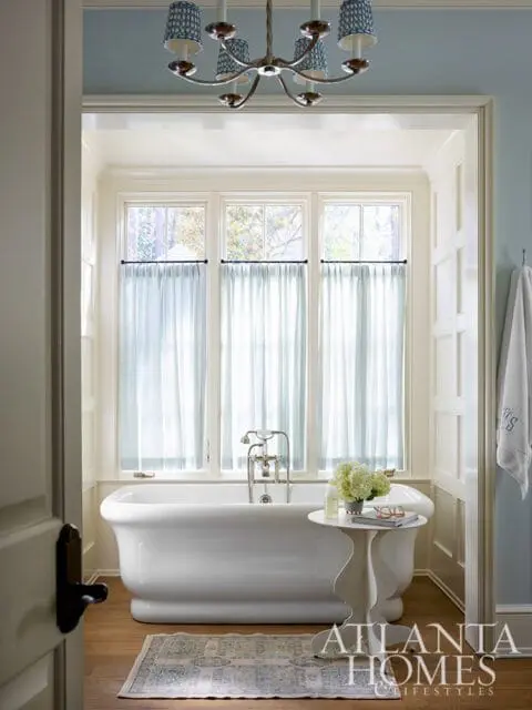 White freestanding bathtub with chrome fixtures, next to a small white table with flowers.