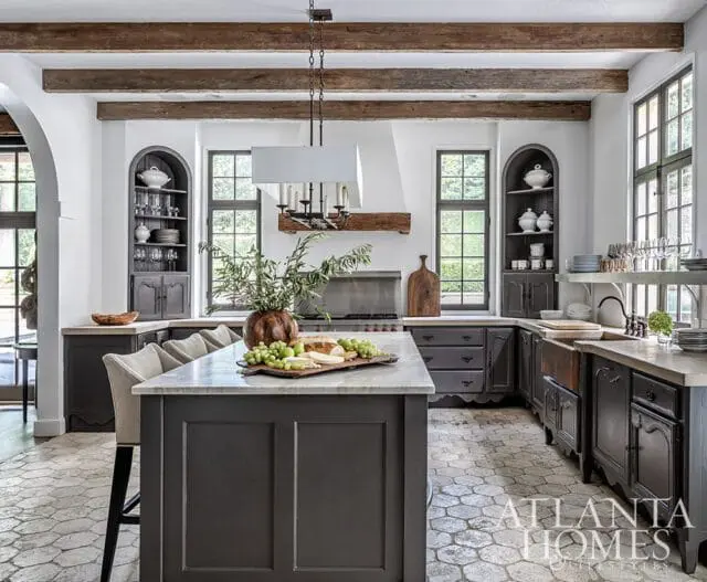 Dark gray kitchen with marble island, stone tile floor, and exposed wood beams.